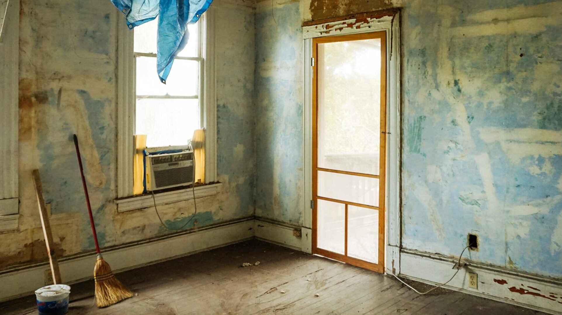 An empty room in an abandoned house with peeling walls and construction tools.